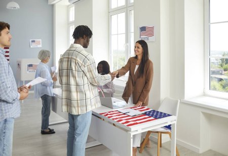 African american young man usa citizen registering at polling station with American flags getting ballot paper and shaking hands with a woman employee working in vote center on election day.
