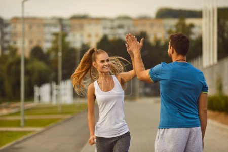 Photo for Woman gives a high five to man coach during a workout session in the city park. This portrait embodies the dynamic connection between trainer and trainee in the pursuit of fitness goals. - Royalty Free Image