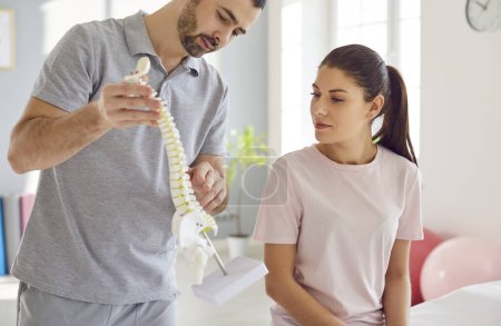 Photo for Portrait of male doctor physiotherapist or orthopedist showing to his woman patient model of spine in rehab clinic giving consultation about scoliosis or spinal problems during medical exam. - Royalty Free Image