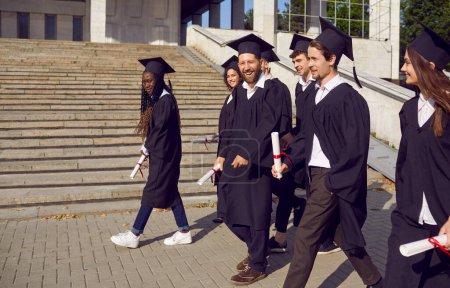 Photo for Group of happy smiling diverse mixed race male and female college or university graduate students in traditional commencement clothes walking joyfully and confidently about campus on graduation day - Royalty Free Image