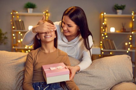 Photo for Smiling young happy mother congratulating her cute teenage girl child on holiday at home. Cheerful woman giving her joyful daughter present gift box sitting on sofa making surprise. - Royalty Free Image