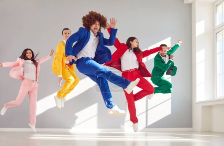 Téléchargez les photos : Habillé en costumes d'affaires colorés groupe de danseurs dansant et sautant en costumes colorés de l'air. Danseurs émotionnels positifs dansant joyeusement Saut et danse drôle émotion positive - en image libre de droit