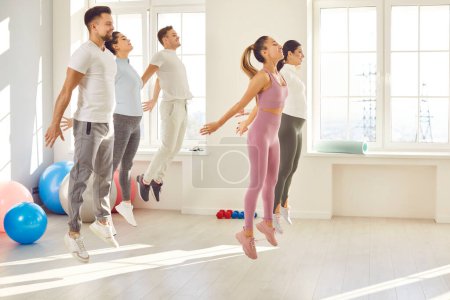 Photo for Young sporty people in jump movement, group exercising in health and fitness club. Friends jumping, training program, recreational service for exercise, sports and effective physical activity indoors - Royalty Free Image