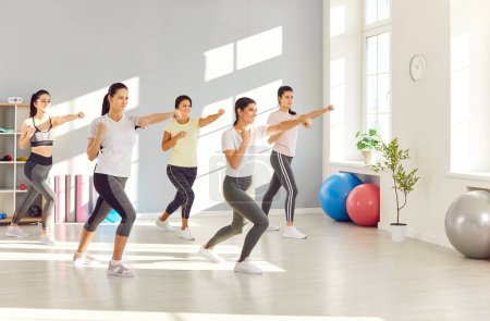 Group of women doing fitness and self defense workout to stay in good shape and be able to defend themselves. Happy sporty powerful ladies exercising at gym, clenching fists, learning fighting moves