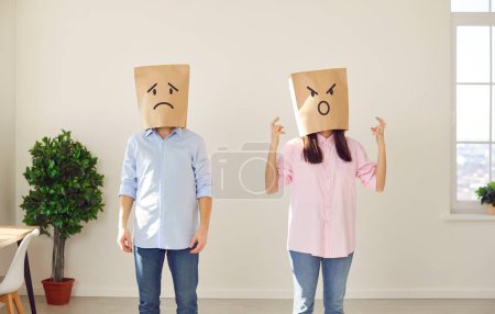 Photo for Faceless woman in bag on head with angry face expression standing near upset unhappy frustrated man in the living room at home. Bad marriage, couple relationships, quarrel and divorce concept. - Royalty Free Image