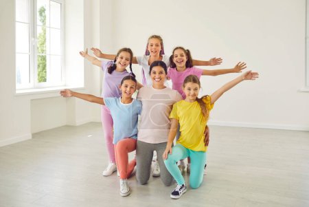 Photo for Portrait of cheerful happy active little girls sitting on the floor with their smiling friendly choreographer woman in choreography class, posing and looking at camera after dance workout. - Royalty Free Image