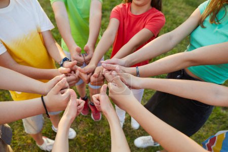 Photo for Top view portrait of a kids friends standing in a circle outdoors and showing thumbs up sign. Hands of boys and girls in summer casual clothes. Childhood, unity and friendship concept. - Royalty Free Image