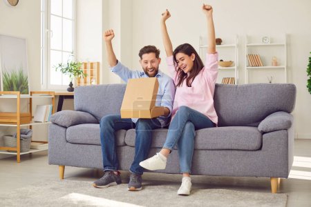 Photo for Excited overjoyed young couple unpacking postal package sitting on sofa in living room at home happy with the purchase and delivery. Man and woman opening parcel. Shopping online concept. - Royalty Free Image