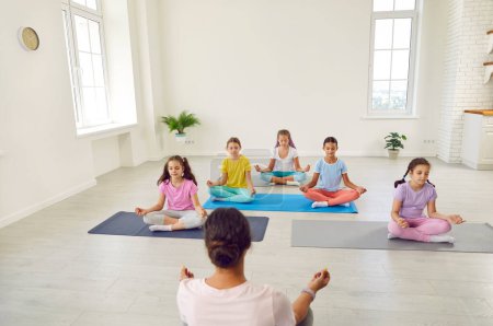 Téléchargez les photos : Adolescentes enfants assis sur le sol avec une enseignante canapé relaxant dans la salle de gym assis sur tapis de yoga dans Lotus pose méditer et faire de l'exercice de yoga. Concept d'entraînement sportif pour enfants. - en image libre de droit