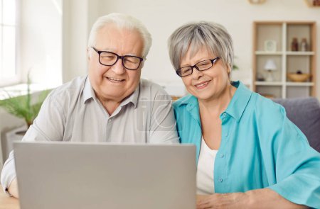 Téléchargez les photos : Joyeux couple de personnes âgées à la retraite utilisant un ordinateur portable pour regarder des films, des achats en ligne et des appels vidéo. Portrait de couple marié âgé caucasien assis à la maison devant l'écran d'ordinateur portable et souriant. - en image libre de droit