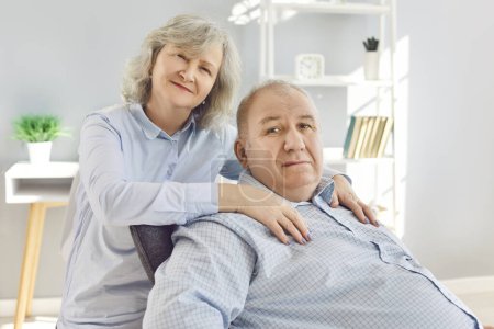 Portrait of a happy senior family couple wife and husband sitting in the living room at home and looking at camera. Two smiling gray-haired retired man and woman enjoying time together on retirement.