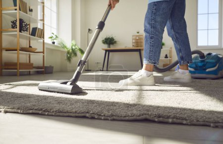 Photo for Cropped photo of woman cleaning with vacuum cleaner carpet in the living room at home. Female janitor vacuuming the floor. Cleaning service, housekeeping, housework and household concept. - Royalty Free Image