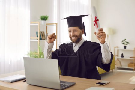 Photo for Distance home graduation ceremony, happy adult male student at laptop wearing cap and gown getting academic degree, online Bachelor, Master certificate study programme, professional education - Royalty Free Image