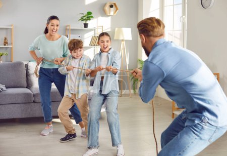 Photo for Happy joyful smiling children playing together with parents in tug-of-war with a rope in the living room at home. Cheerful young family having fun with kids indoors. Happy family and leisure concept. - Royalty Free Image