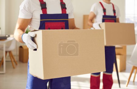 Photo for Close up of a man mover worker from professional moving service in uniform holding a cardboard box in hands standing in new apartment. Move, relocation, delivery and moving day concept. - Royalty Free Image