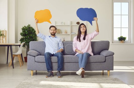 Photo for Speech bubble for thoughts. Young couple is sitting on sofa and each of them is holding colored speech bubble. Concept of communication in relationship, exchange of ideas and interaction of couple. - Royalty Free Image