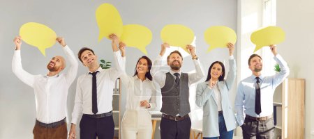 Photo for Young cheerful smiling business people employees holding yellow paper clouds standing in office. Men and women with empty blank speech bubble for thoughts standing in a row. Idea concept - Royalty Free Image