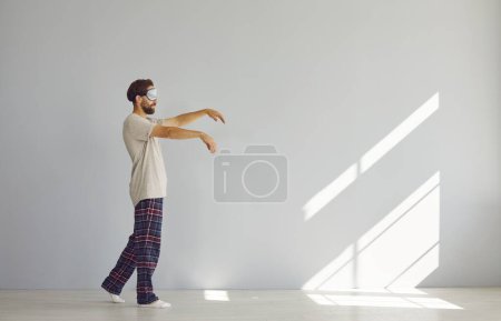 Photo for Full length portrait of young sleepwalker man in pajamas suffering from sleepwalking in sleep mask isolated on gray wall background. Somnambulism, insomnia and sleep problems concept. - Royalty Free Image