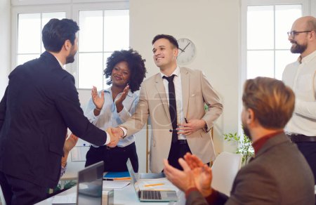 Photo for Team of business professionals applauding after successful handshake between two colleagues. Employees greet two colleagues with tight handshake, indicating successful partnership or deal. - Royalty Free Image