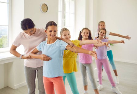 Photo for Learning new dance. Teacher of childrens dance school helps preteen girls perform choreographic exercises. Choreographer communicates with little dancers. Concept of active lifestyle of children - Royalty Free Image