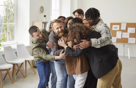 Diversos grupos de personas en una oficina se reúnen en un abrazo, simbolizando el apoyo, la unidad y una bienvenida. Cada individuo contribuye a la fuerza del equipo, formando un símbolo de trabajo en equipo.