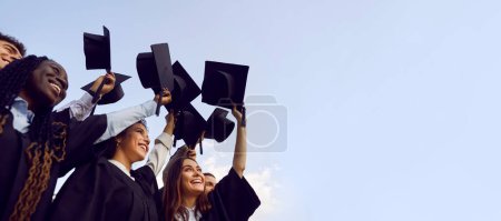 Foto de Grupo de estudiantes de secundaria, universitarios o universitarios multiétnicos felices divirtiéndose en el día de la graduación y levantando sus sombreros de graduación para despejar el cielo azul. Copiar espacio banner fondo - Imagen libre de derechos