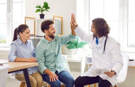 Happy family couple visit doctor together. Cheerful, smiling married man and woman give high five to their doctor. Health care, pregnancy planning, IVF treatment, success concept