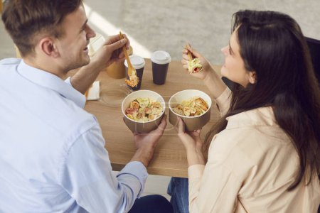 Cozy home lunch break. Happy young man and woman are talking happily while enjoying delicious takeaway. Joyful couple sharing food and thoughts during home dinner, with cardboard containers and drinks