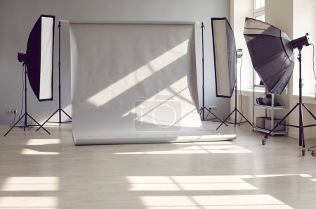 Photo for Interior of an empty modern photo studio with professional lighting equipment of rectangular softbox and octabox against gray background prepared for photography work photo session. - Royalty Free Image