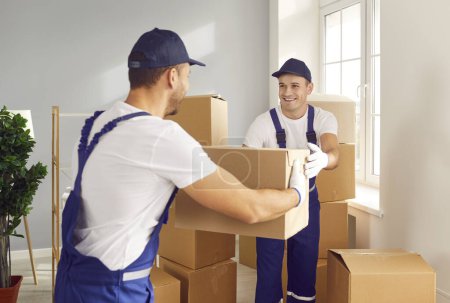 Photo for Happy workers from the moving service put belongings in the new apartment. Two smiling men from the delivery company put cardboard boxes inside the house where their clients are relocating - Royalty Free Image