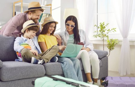 Photo for Young happy family booking tickets online via laptop in internet sitting on sofa in living room at home together. Parents with kids waiting for summer vacation trip. Travel concept. - Royalty Free Image