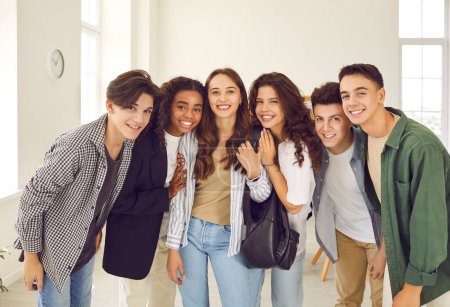 Foto de Retrato de un grupo de felices y diversos estudiantes de secundaria sonrientes y compañeros de clase con ropa casual parados juntos en una fila y mirando alegre y positivamente a la cámara y abrazando. - Imagen libre de derechos