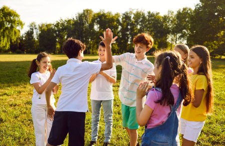 Téléchargez les photos : Groupe d'enfants heureux s'amuser et se donner cinq hauts quand ils se rencontrent tout en marchant dans le parc d'été dans la nature. Les enfants joyeux amis rient à l'extérieur. Concept d'amitié. - en image libre de droit