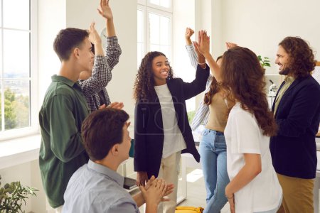 Photo for Group of happy teenage school students together with teacher having fun in classroom. Smiling African American girl high fives her friend while others clap hands. Education, teamwork, success concept - Royalty Free Image