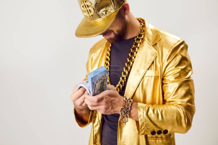 Photo for Rich man in a golden business suit counting cash against a white background. This image symbolizes money wealth, success, and financial prosperity, reminiscent of a successful rapper. - Royalty Free Image