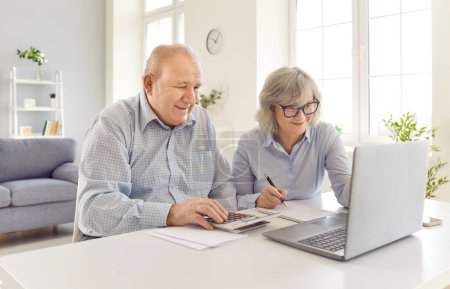 Pareja de ancianos trabajando juntos en casa, usando una computadora portátil para administrar facturas, pagos, deudas y contabilidad. Son felices y sonrientes, mostrando responsabilidad financiera y trabajo en equipo en la gestión de las finanzas.