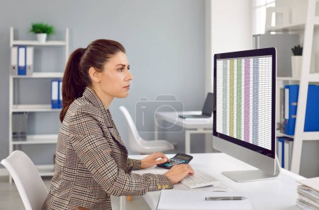 Photo for Female accountant working in office. Accountant entrepreneur works with spreadsheet and calculator to calculate financial data report. Serious woman at her workplace in office. - Royalty Free Image