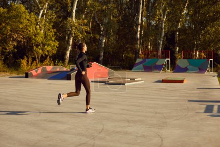 Foto de Vista trasera de una hermosa mujer joven y deportiva corriendo en un campo deportivo y una rampa de skate en el parque de la ciudad. Deporte, ejercicio, fitness, bienestar, concepto de entrenamiento - Imagen libre de derechos