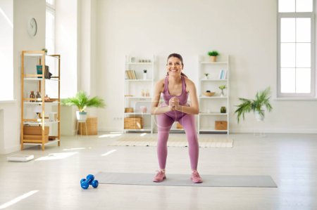 Portrait of a sporty athletic young woman exercising at home on the floor. Young girl doing sits up exercises in the living room. Fitness, healthy lifestyle and home training concept.