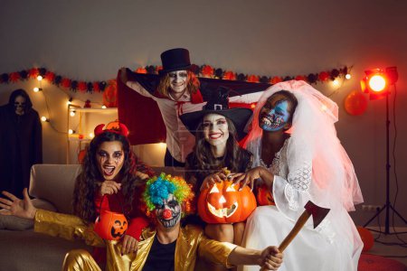 Portrait of smiling diverse young people in scary horror costumes celebrate Halloween in decorated home together. Happy multiethnic friends on masquerade enjoy all saint eve party celebration.