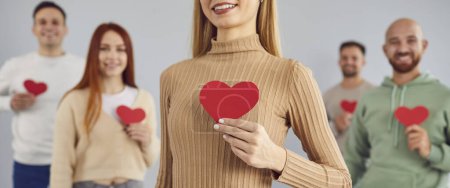 Photo for Group of young smiling people holding paper red symbol heart, love, like, care, cardio symbol. Loving relationships, understanding of adult attachment, secure people feeling comfortable with intimacy - Royalty Free Image