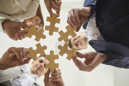 Photo for Business colleagues holding puzzles as symbol of cooperation, brainstorming and teamwork. Happy team of people standing in circle. Business solutions, success and strategy concept. Bottom view. - Royalty Free Image