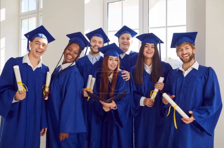Divers groupes de jeunes gens joyeux portant des robes de graduation bleues à l'intérieur regardant joyeusement la caméra avec des diplômes dans les mains. Heureux portrait d'étudiants diplômés. Concept d'éducation.