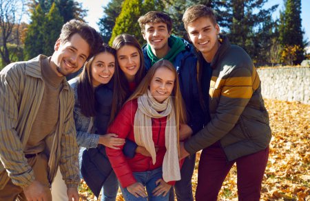 Photo for Portrait of a group of happy friends walking in the autumn park. Young caucasian people girls and boys looking at the camera and smiling cheerfully outdoors. Friendship and togetherness concept. - Royalty Free Image