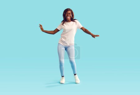 Téléchargez les photos : Portrait d'une jeune afro-américaine drôle cool avec expression joyeuse du visage dansant portant des vêtements décontractés isolés sur fond bleu turquoise. Heureuse femme excitée s'amuser en studio. - en image libre de droit