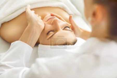 Pure relaxation and joy of spa treatments as a positive woman indulges in a facial massage procedure by a cosmetologist in a beauty salon. The image captures the essence of care and face treatment.