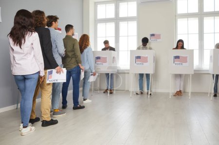 Group of diverse american people voters standing in queue holding ballot paper at electoral center on election day and putting their ballots in bin in voting booth. Democracy and election concept