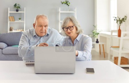 Älteres Ehepaar arbeitet zu Hause gemeinsam an einem Laptop. Rechnungen, Rechnungen verwalten und möglicherweise Geldfragen, Geldanlagen, Renten oder Schulden diskutieren, Engagement und Teamwork zeigen.
