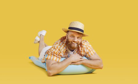Hombre feliz en ropa de vacaciones de playa, sombrero de sol de paja, turista acostado en el colchón inflable de verano. Tiempo libre, recreación relajarse, viajando hombre veraneante descansando en vacaciones, fondo amarillo brillante 