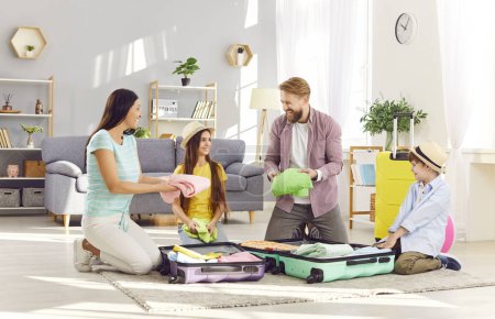 Padres jóvenes felices con dos niños y niñas haciendo maletas preparándose para el viaje de vacaciones de verano sentados en el suelo en casa juntos. Viajes, vacaciones en familia y concepto de viaje.